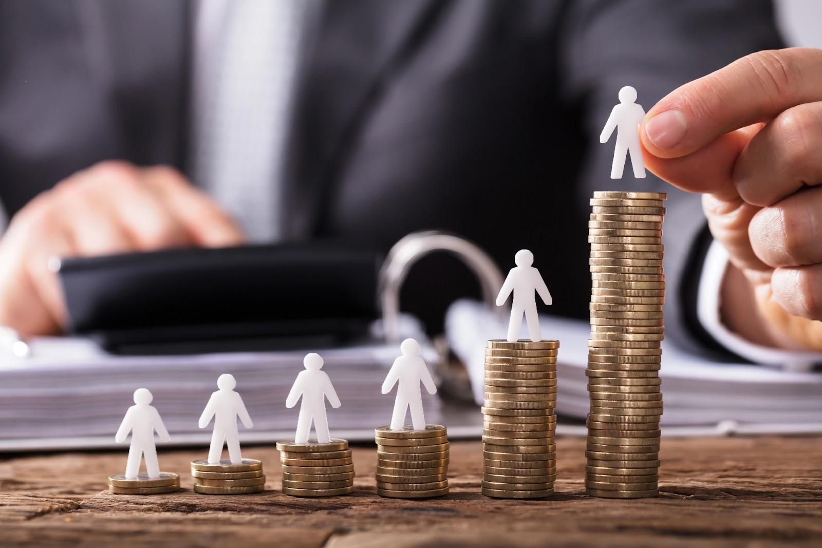  Small plastic figures in the shape of people standing on stacks of coins.