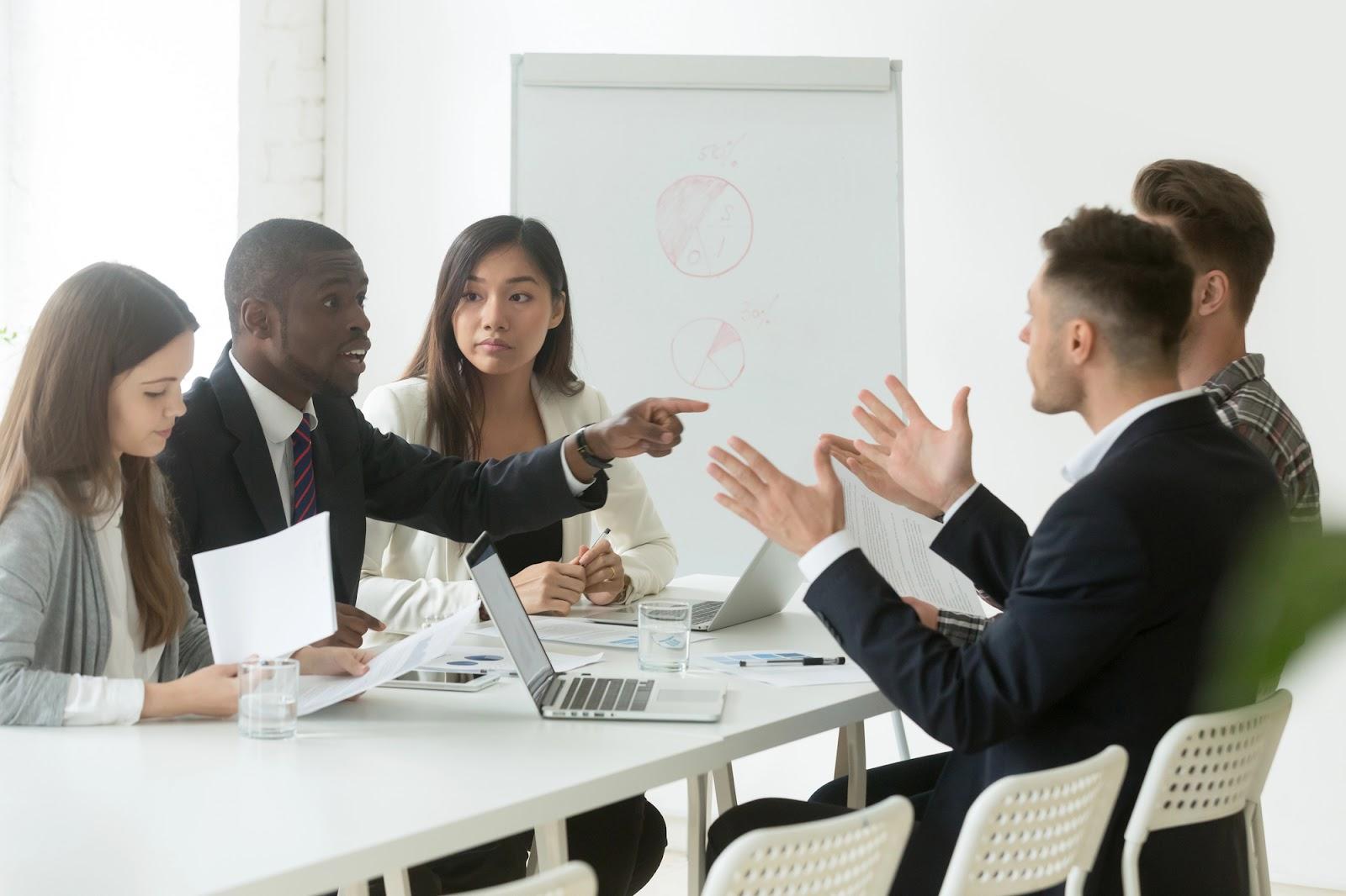 Two business teams seated on opposite sides of a conference table; discussing whether a breach should be considered a minor violation vs. a material violation of the contract terms. 